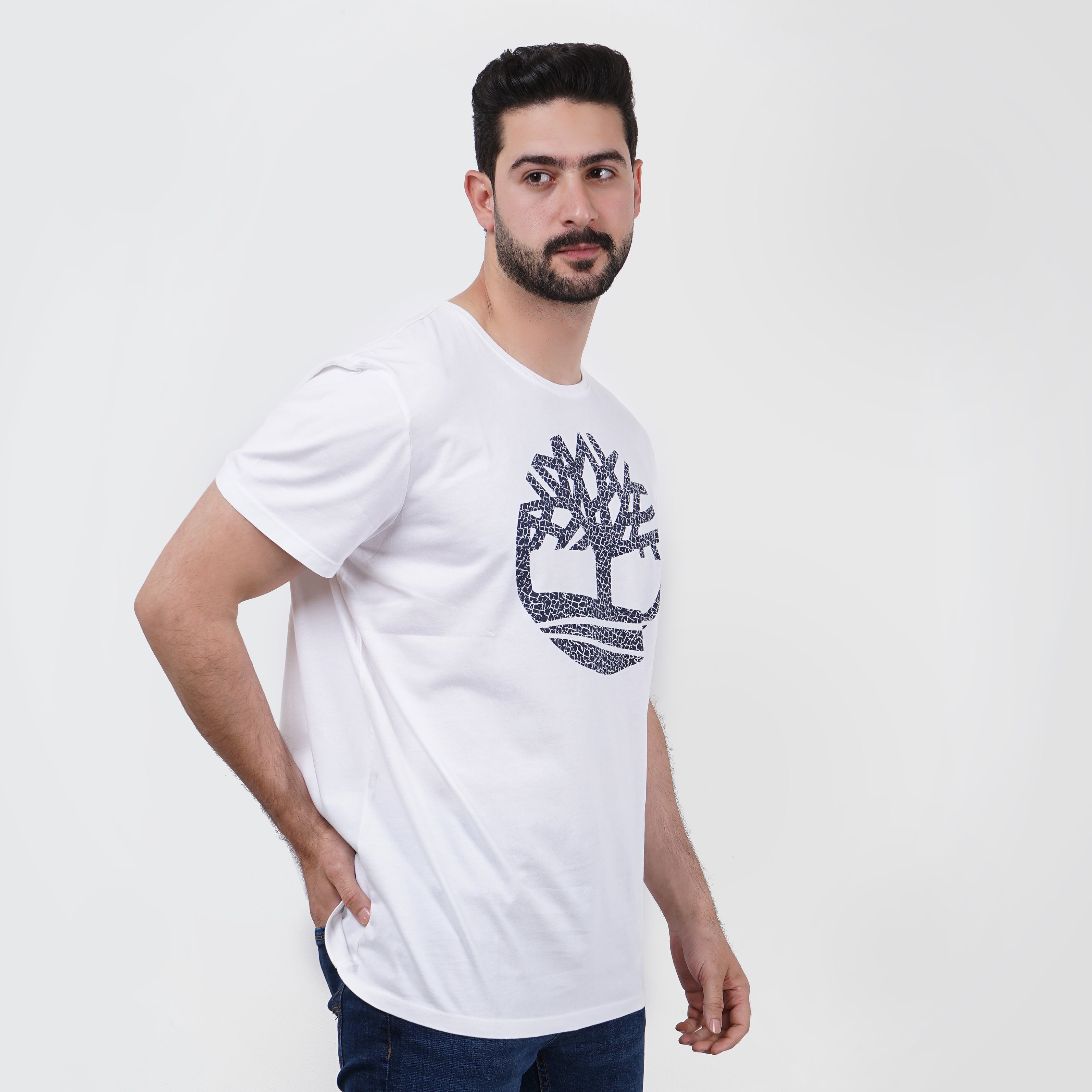 Man posing in white graphic Timberland t-shirt with abstract logo design, casual fashion.