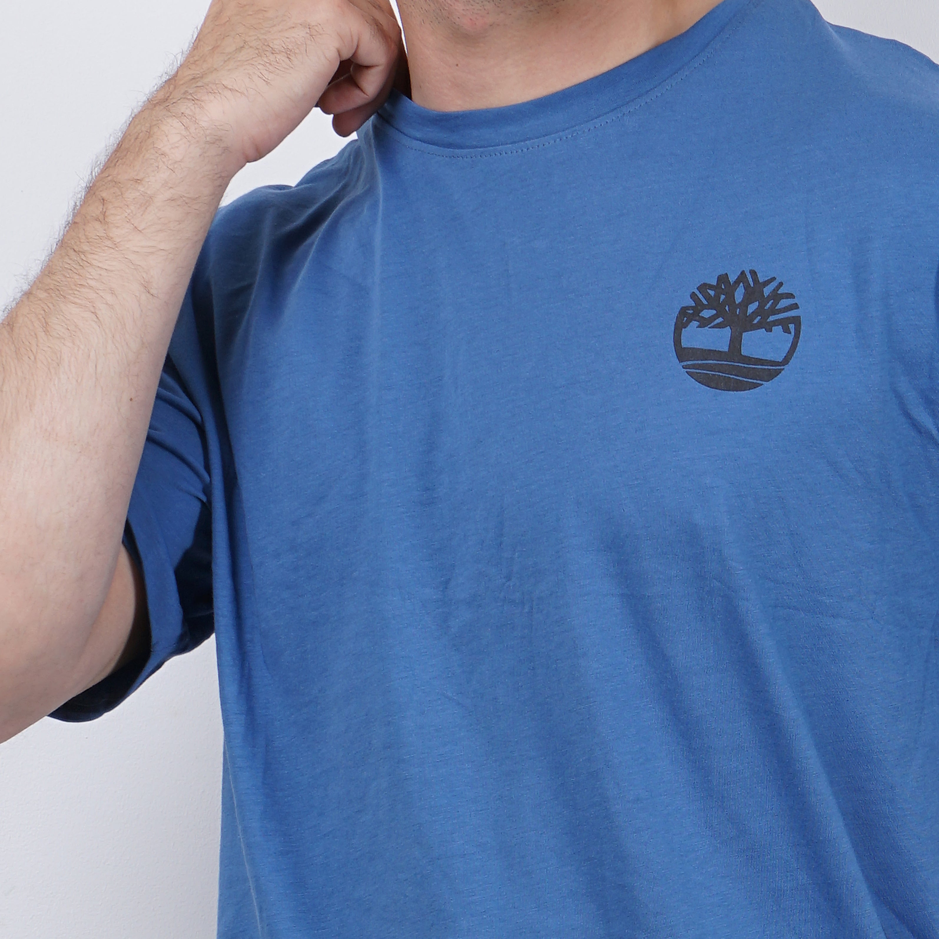 Man in blue t-shirt with Timberland logo, posing with hand on neck.