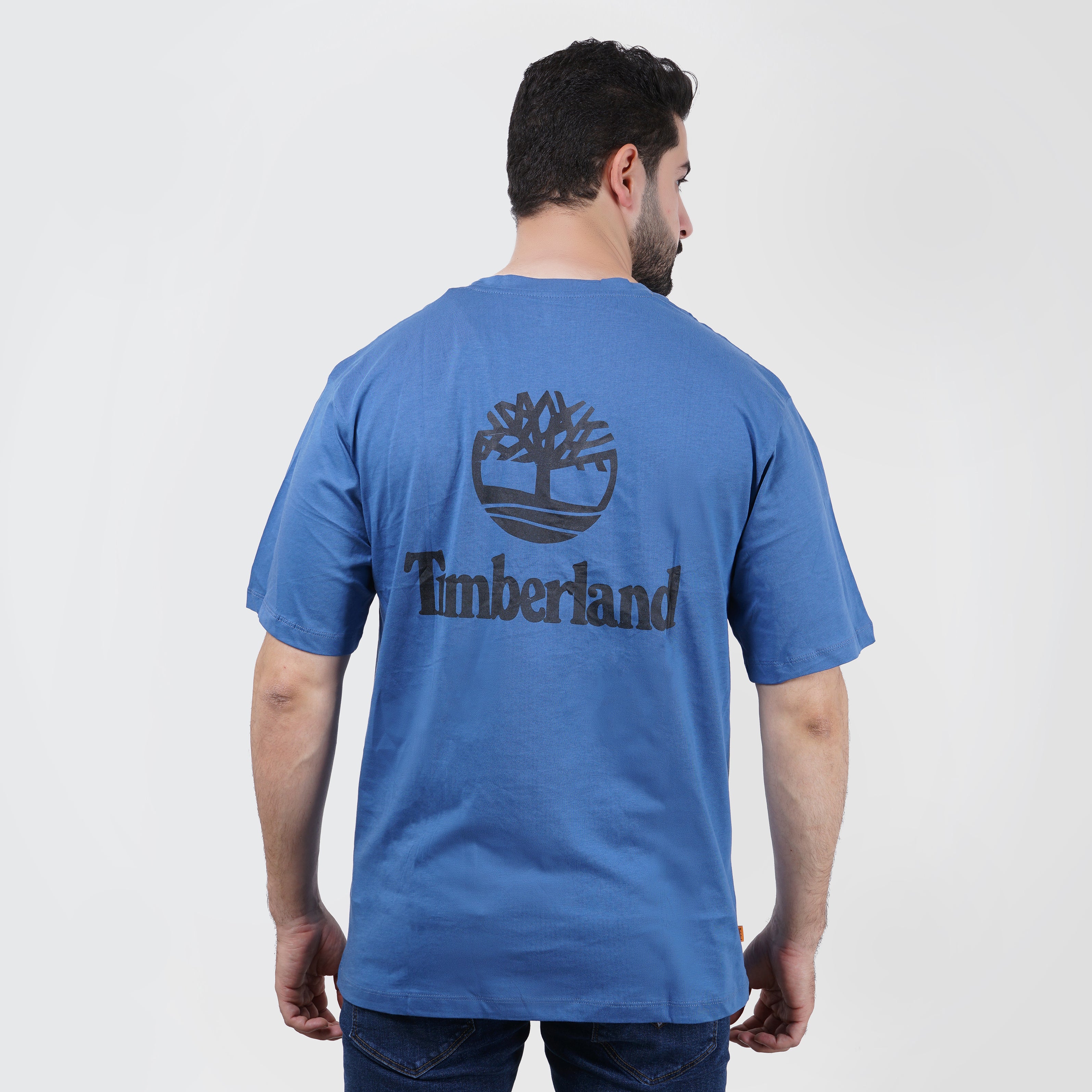 Man wearing blue Timberland logo t-shirt, rear view, on white background.