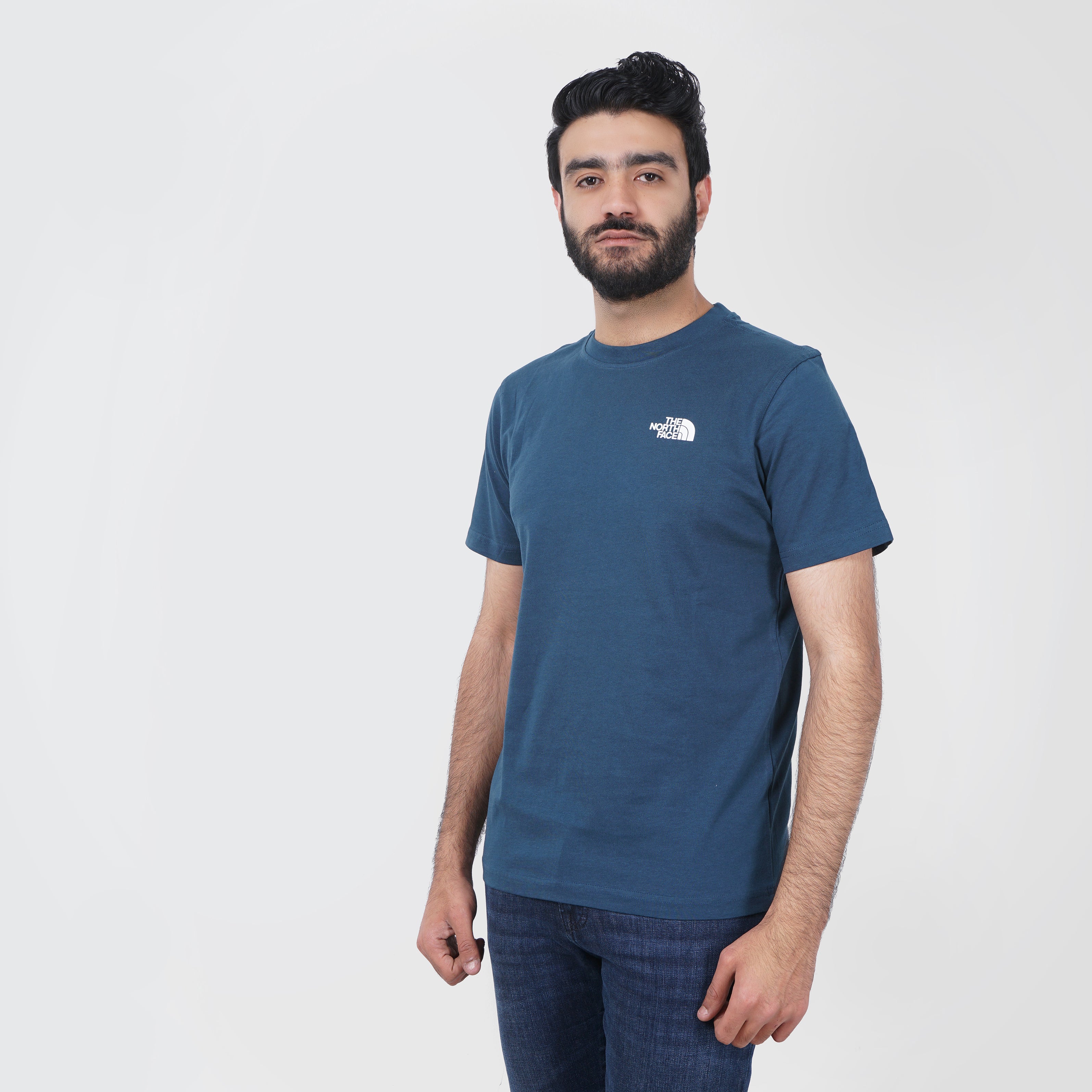 Man in navy blue North Face t-shirt standing against white background.