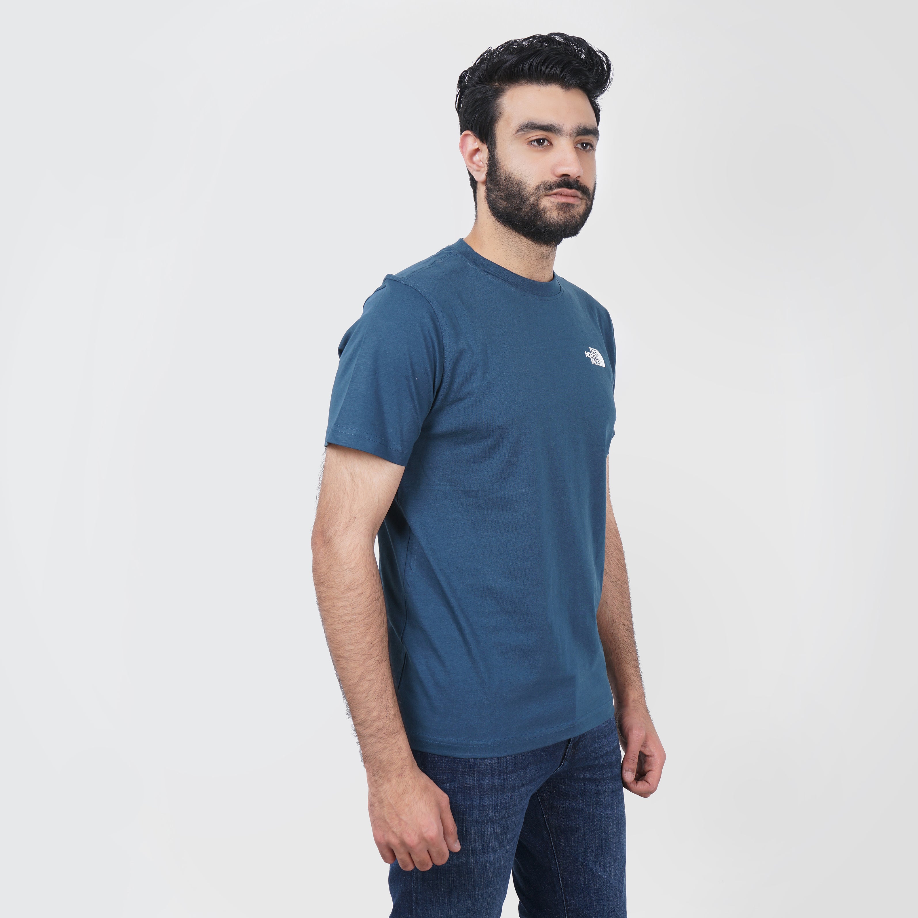 Man in a blue North Face t-shirt and jeans posing against a white background.