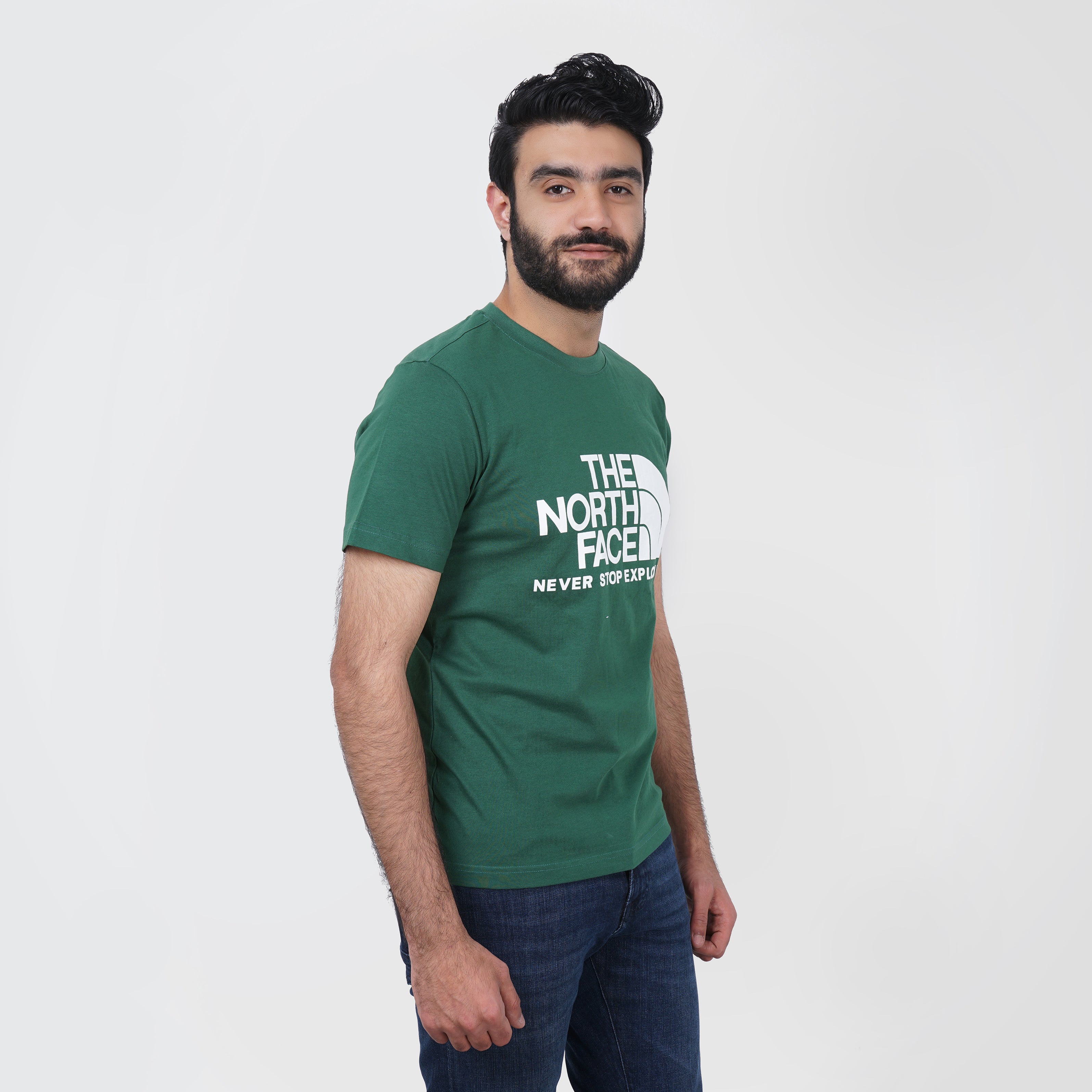 Man in green t-shirt with The North face logo, standing against a white background.