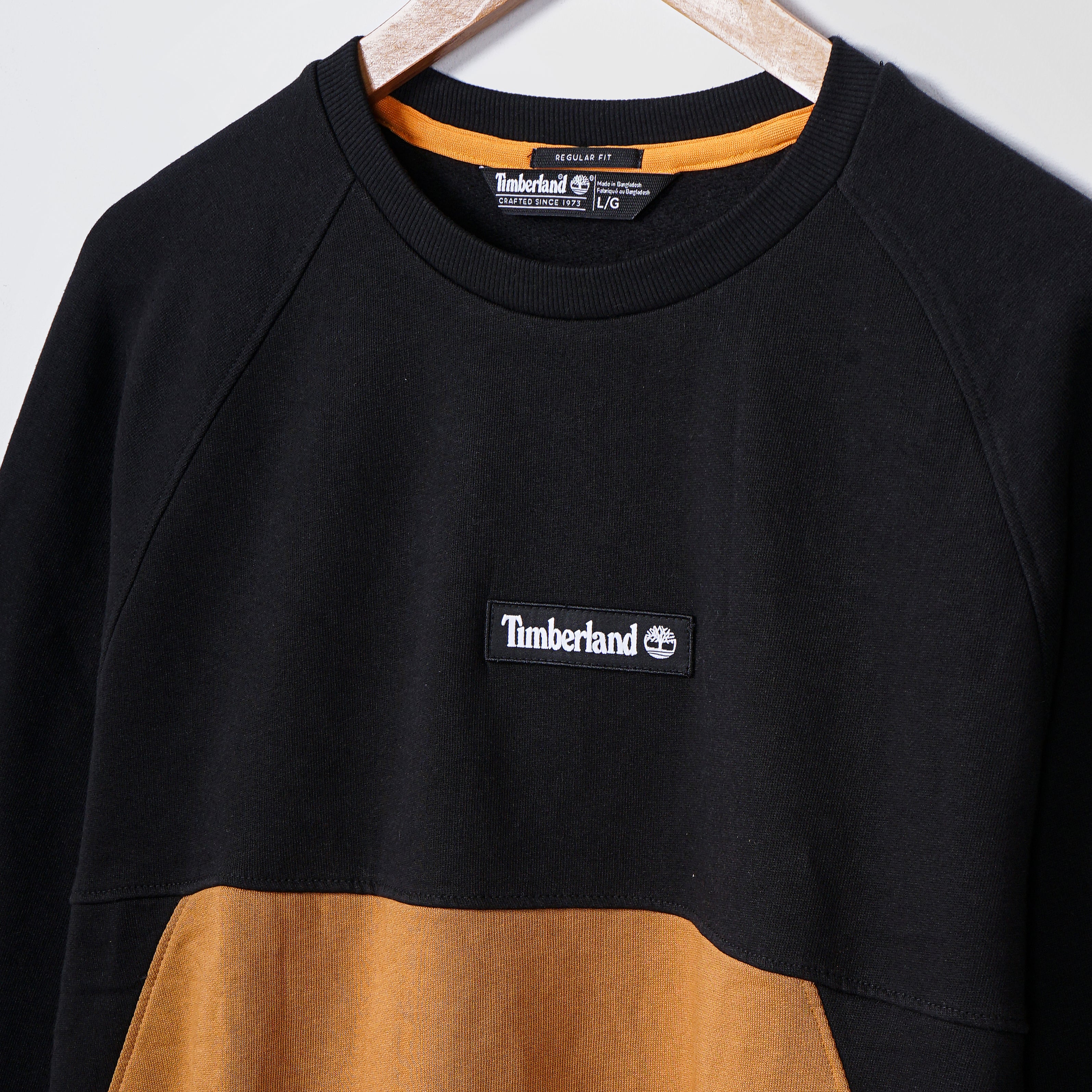 "Black and tan Timberland sweater on hanger highlighting logo for fashion retail."