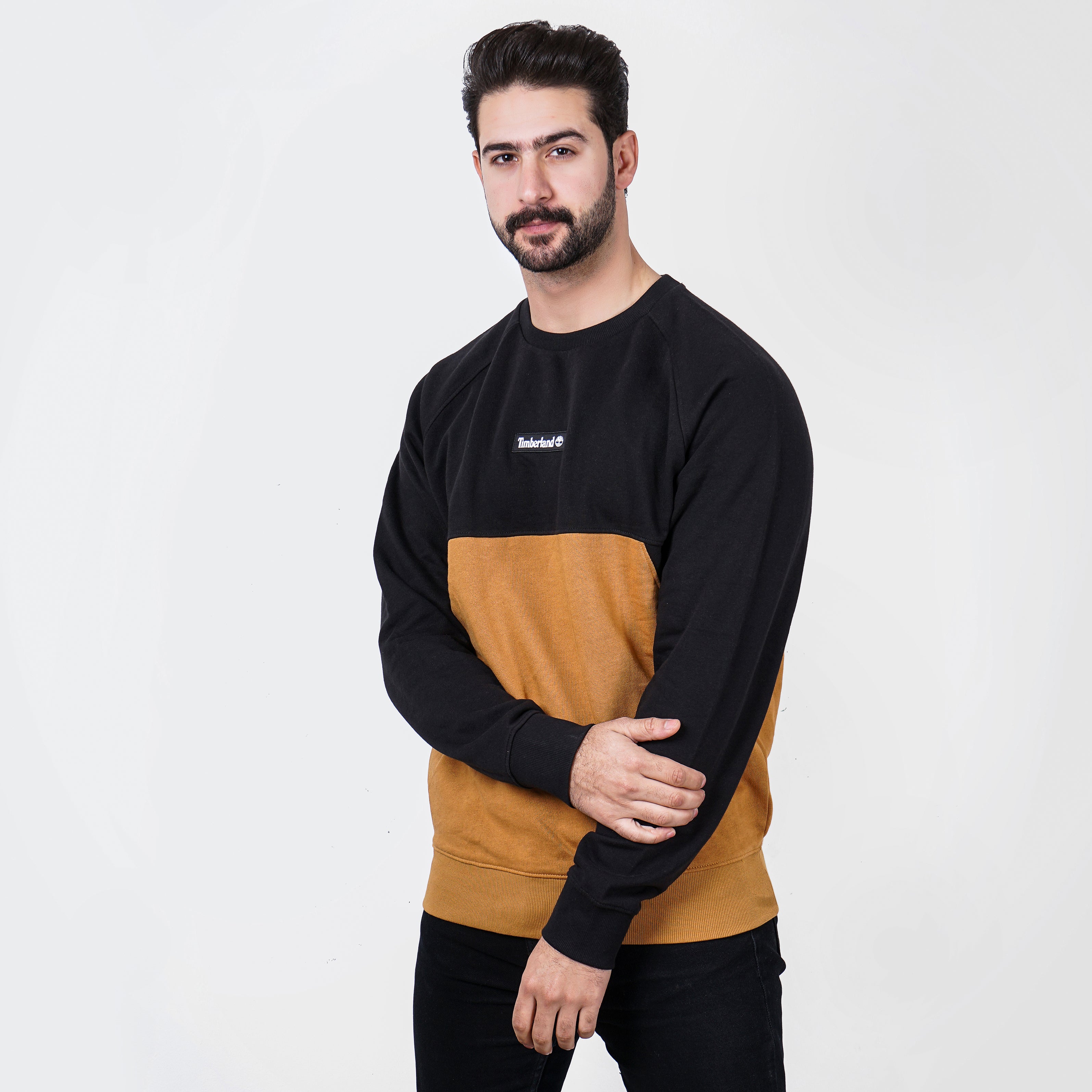 Man in black and tan color-blocked Timberland sweater posing against white background.