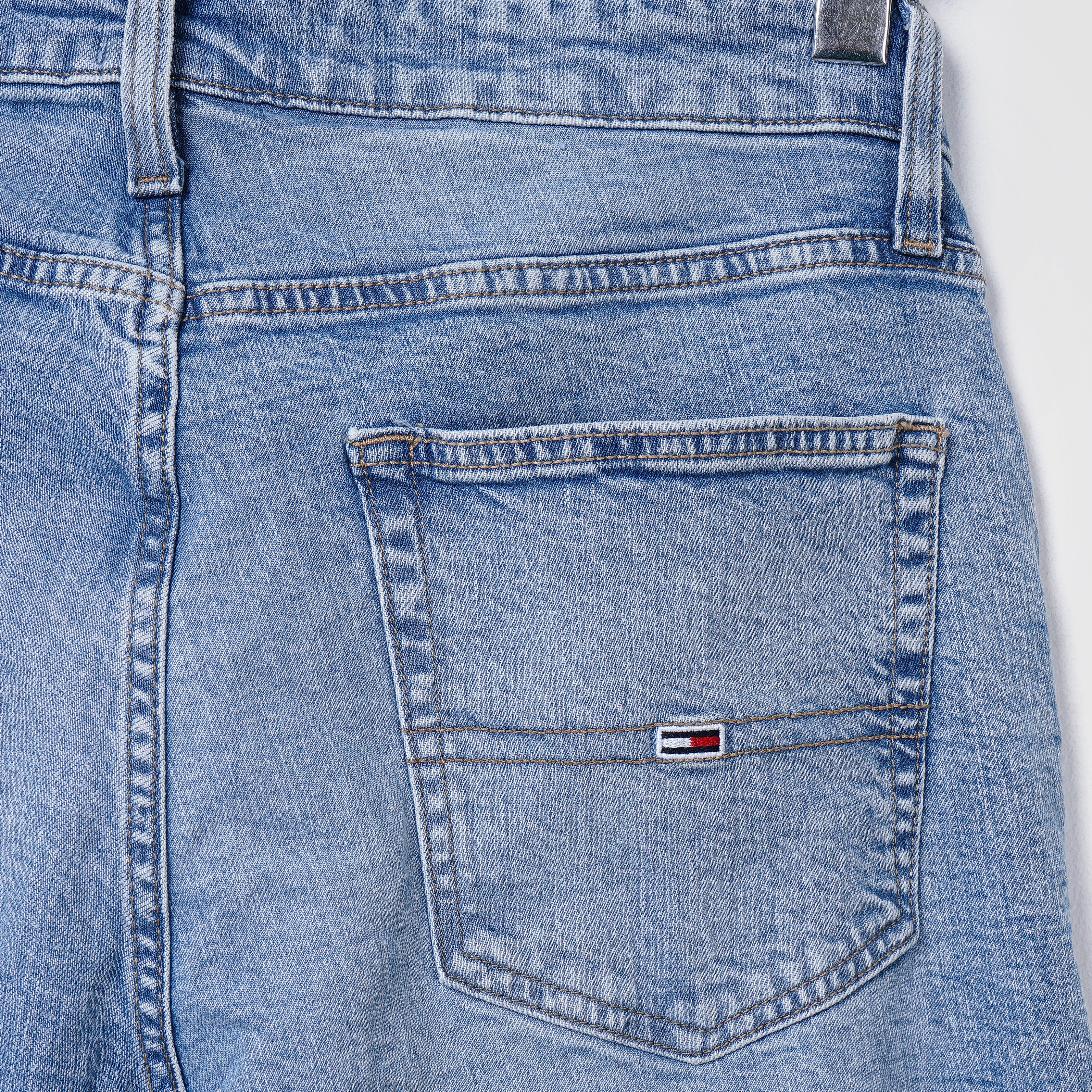 Close-up of back pocket of light wash denim TOMMY jeans.