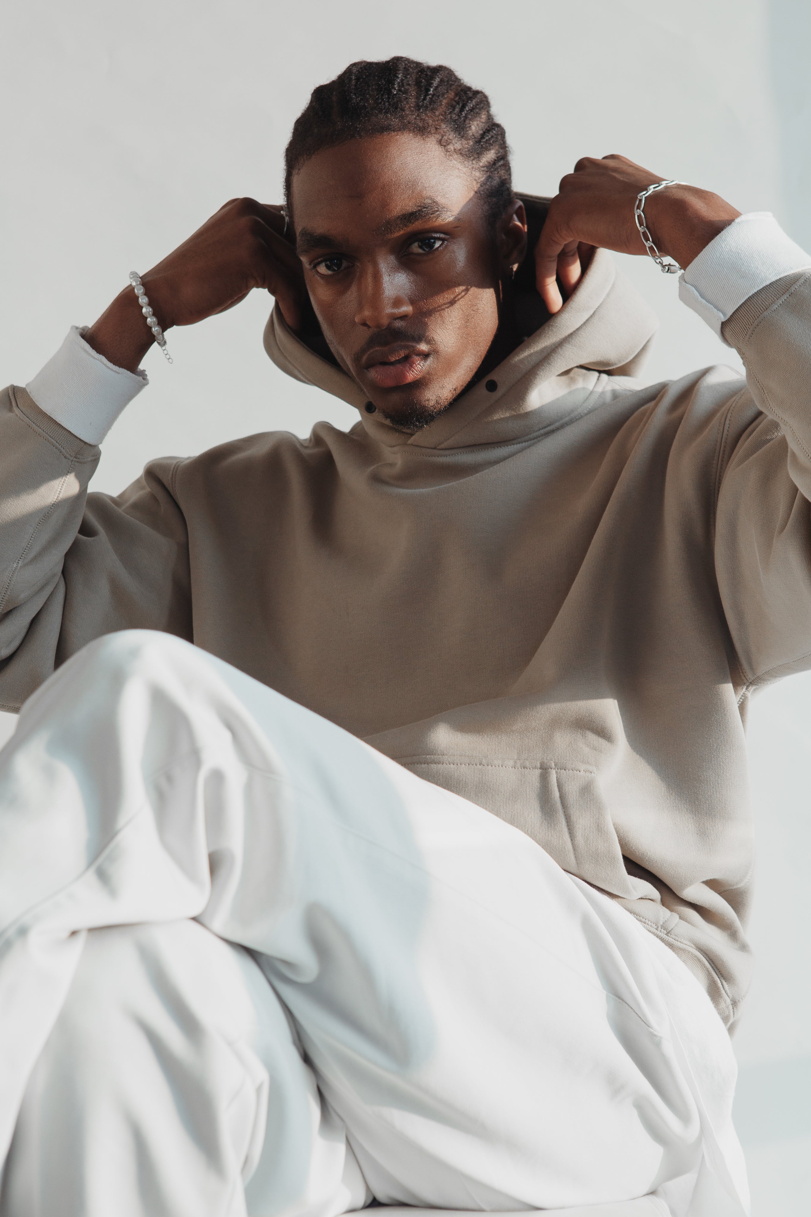 Stylish man in beige hoodie posing with hands on head and white pants