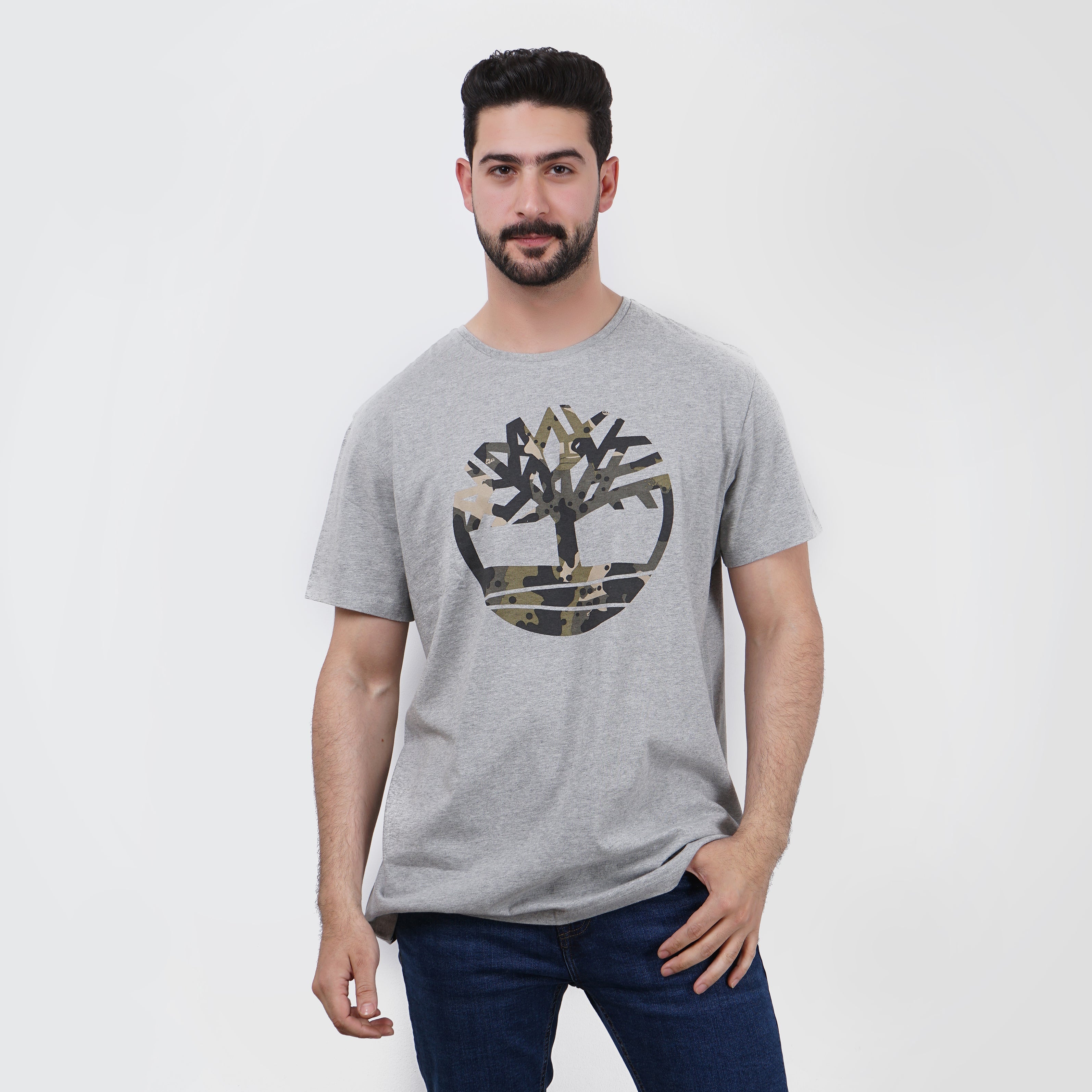 Man modeling a gray camouflage Timberland graphic t-shirt and blue jeans.